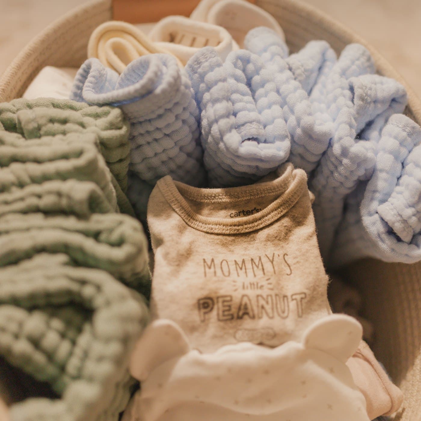 Baby clothes, toys and accessories laid out on a pale wooden surface